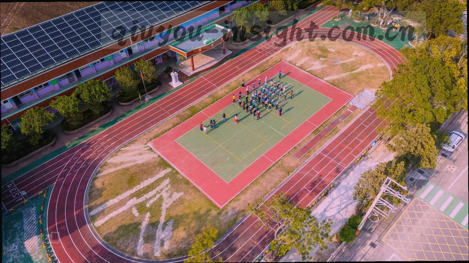 黄昏下城市业余球场的外景，草皮与围网形成规则线条，边灯刚刚亮起